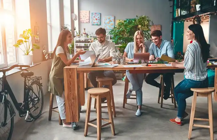 Imagen de grupo de personas en una junta creativa de estrategia de marca dentro de una oficina luminosa con vista hacia la calle.